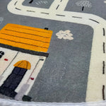 Load image into Gallery viewer, Close up of a house and road illustrations on a children's round carpet depicting a small town design
